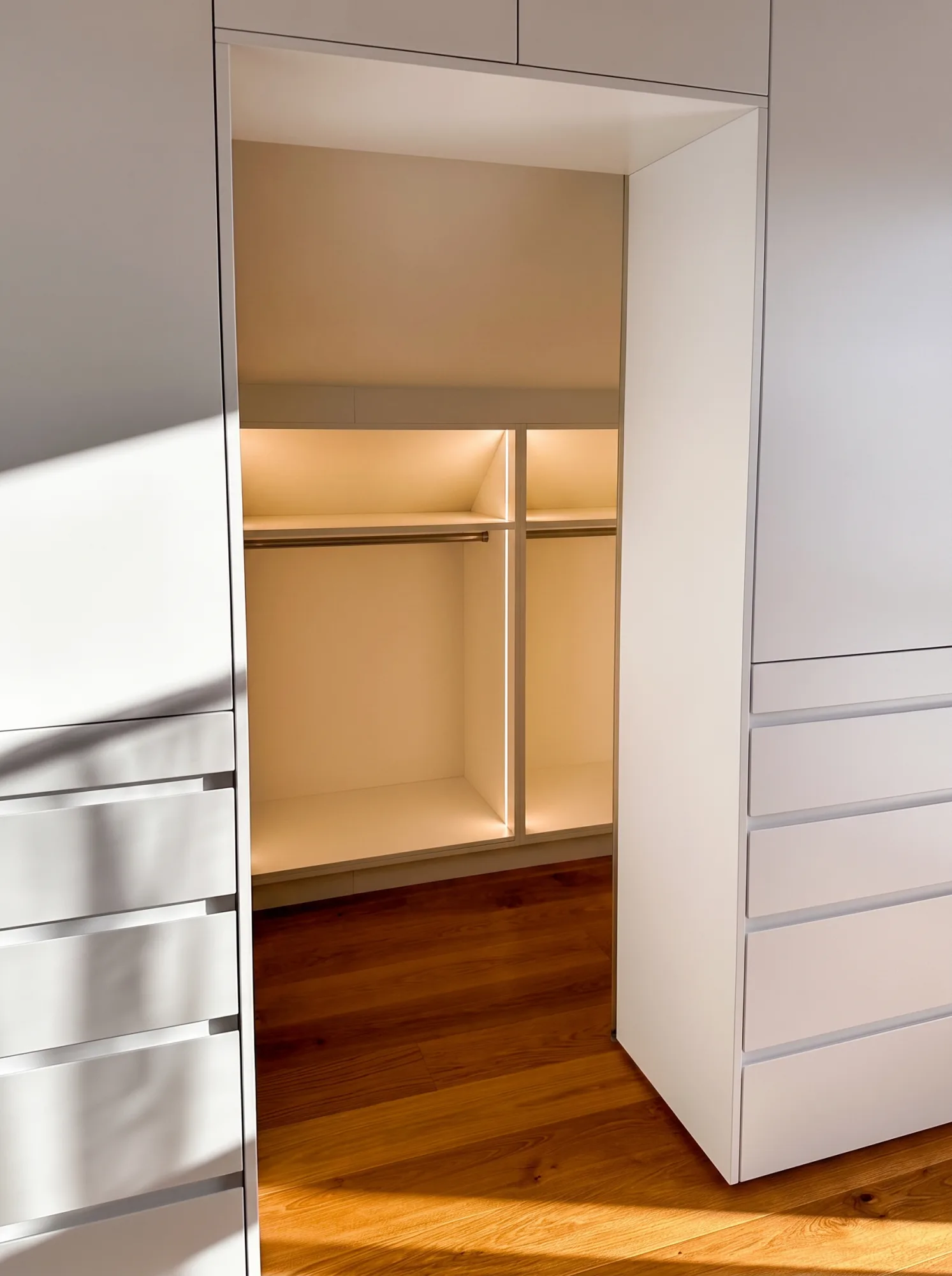 Blick in die beleuchtete Kleiderstange einer begehbaren Ankleide nach Maß