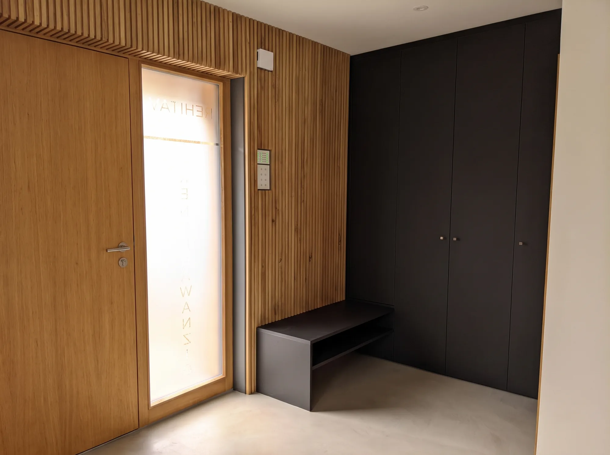 Garderobe nach Maß im Eingangsbereich mit Akustik-Holzwand, schwebender Sitzbank und schwarzem Garderobenschrank