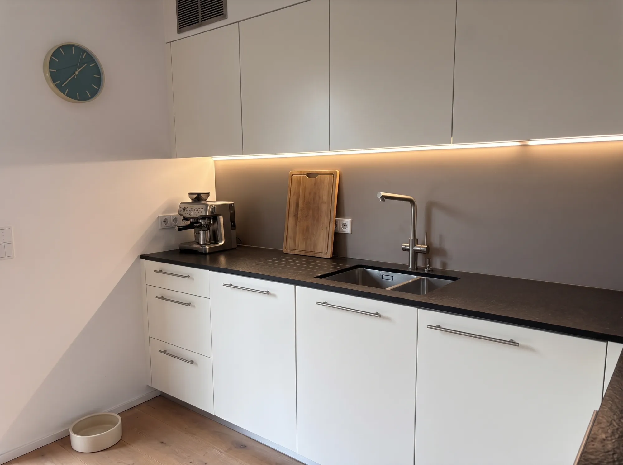 Moderne weiße Küche nach Maß mit Griffleisten, dunkler Steinarbeitsplatte und LED-Beleuchtung